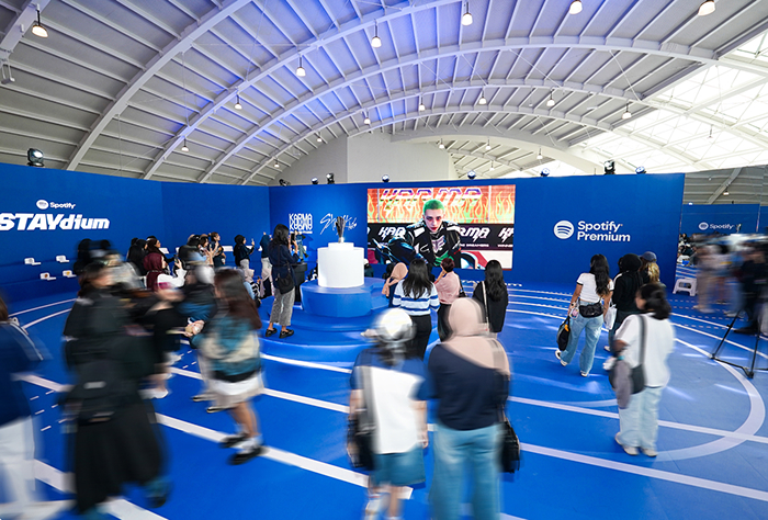 Foto para penggemar di acara pop-up, dengan elemen branding STAYdium dan orang-orang yang diburamkan